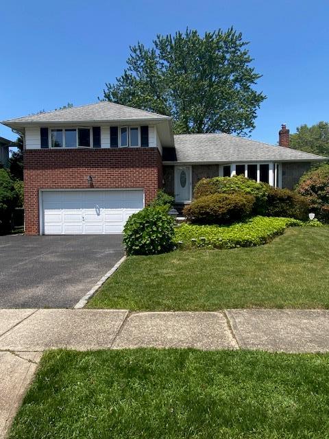16 Clearland Rd, Syosset, NY 11791 - view of front of property with brick siding, driveway, an attached garage, and a front lawn