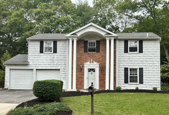 44 Woodbine St, Coram, NY 11727 - greek revival house featuring asphalt driveway, a front lawn, a shingled roof, and view of scattered trees
