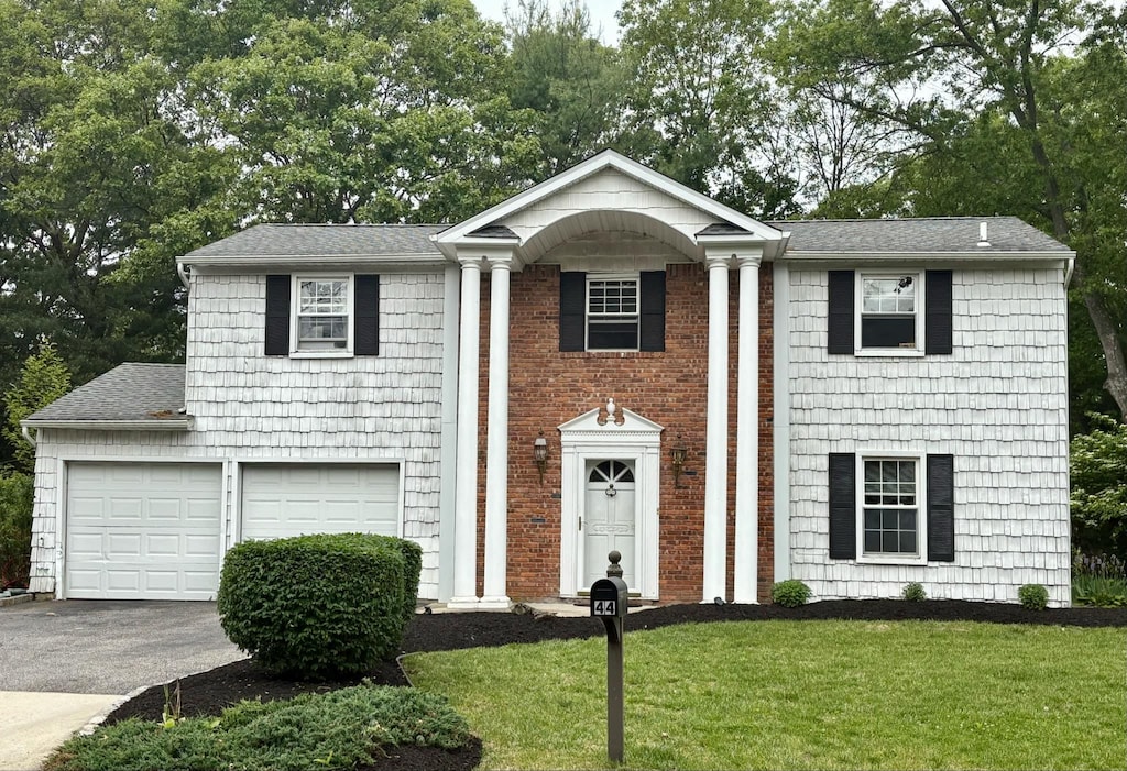 44 Woodbine St, Coram, NY 11727 - neoclassical / greek revival house featuring asphalt driveway, a front yard, a shingled roof, and view of wooded area