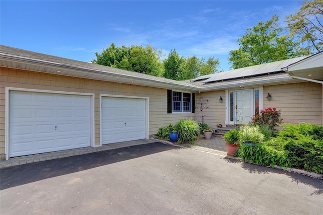 12 Bridle Path Ln, Port Jefferson, NY 11777 - doorway to property with driveway, roof mounted solar panels, a garage, and a shingled roof