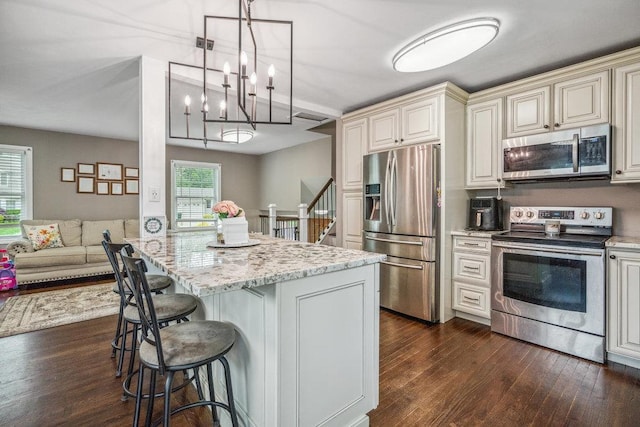 12 Pleasant Pl, Farmingville, NY 11738 - kitchen featuring stainless steel appliances, cream cabinetry, light stone countertops, dark wood-type flooring, and a kitchen breakfast bar