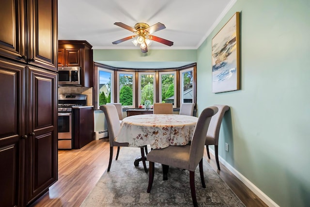 9 Duke St, North Babylon, NY 11703 - dining room featuring a baseboard heating unit, light wood finished floors, crown molding, a ceiling fan, and baseboards