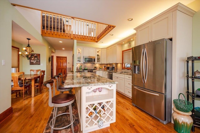 991 W Park Ave, Long Beach, NY 11561 - kitchen with stainless steel appliances, light wood-style floors, light stone countertops, a chandelier, and a kitchen bar