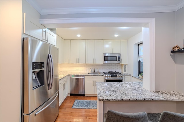 32 Manchester Rd Unit # B26, Eastchester, NY 10709 - kitchen featuring appliances with stainless steel finishes, white cabinets, light wood finished floors, backsplash, and light stone counters