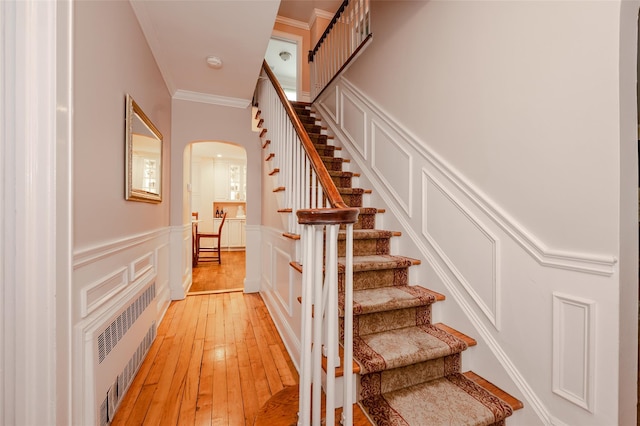 70 Loines Ave, Merrick, NY 11566 - stairway featuring arched walkways, hardwood / wood-style flooring, a decorative wall, crown molding, and a wainscoted wall