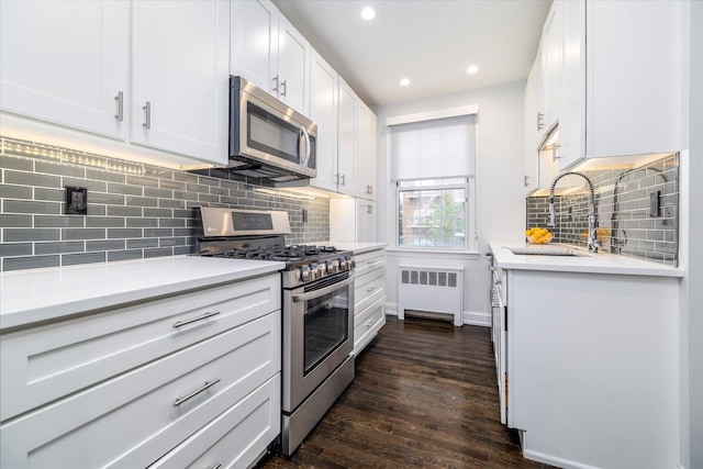70 S Park Ave Unit 114, Rockville Centre, NY 11570 - kitchen with stainless steel appliances, radiator heating unit, a sink, light countertops, and white cabinetry