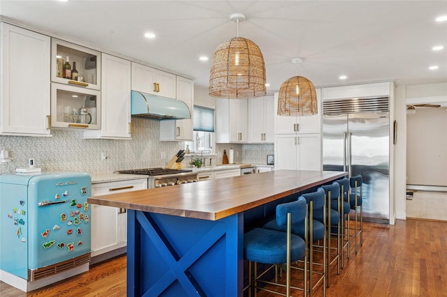 931A Oceanfront St, Long Beach, NY 11561 - kitchen with butcher block counters, stainless steel built in refrigerator, under cabinet range hood, wood finished floors, and white cabinetry