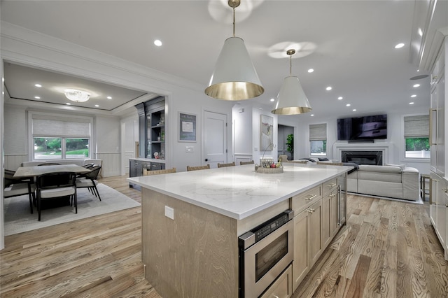 9 Wyndham Way, Port Washington, NY 11050 - kitchen with stainless steel microwave, open floor plan, light wood-style floors, a kitchen island, and a glass covered fireplace