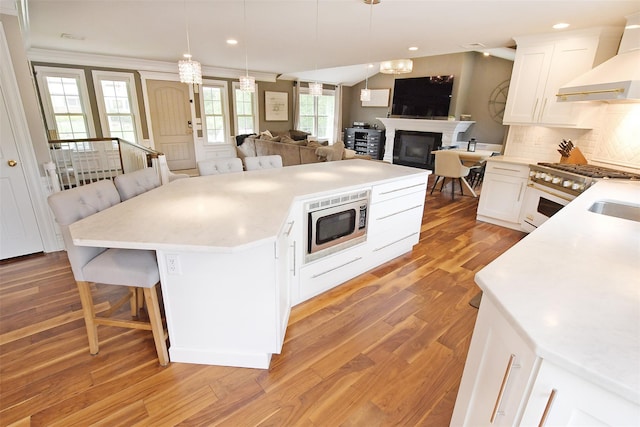 213 Glenwood Ln, Port Jefferson, NY 11777 - kitchen featuring wall chimney range hood, stainless steel microwave, open floor plan, white cabinets, and a kitchen bar