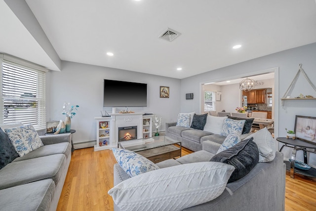130 W 7th St, Deer Park, NY 11729 - living area featuring baseboard heating, light wood finished floors, a chandelier, recessed lighting, and a warm lit fireplace