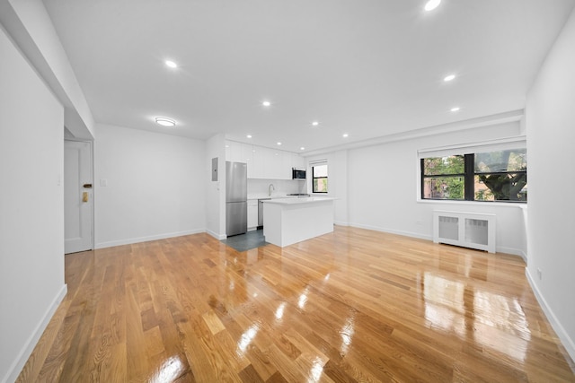 25-10 31st Ave Unit 2M, Astoria, NY 11106 - unfurnished living room featuring radiator heating unit, light wood-style floors, recessed lighting, and baseboards