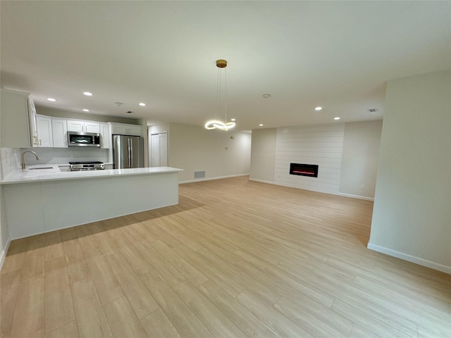 19 Erin Ln, East Setauket, NY 11733 - unfurnished living room featuring a large fireplace, light wood-type flooring, baseboards, recessed lighting, and a sink
