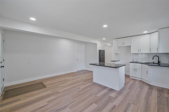 71 Cinnamon St, Central Islip, NY 11722 - kitchen with a sink, light wood-style floors, dark countertops, decorative backsplash, and white cabinetry