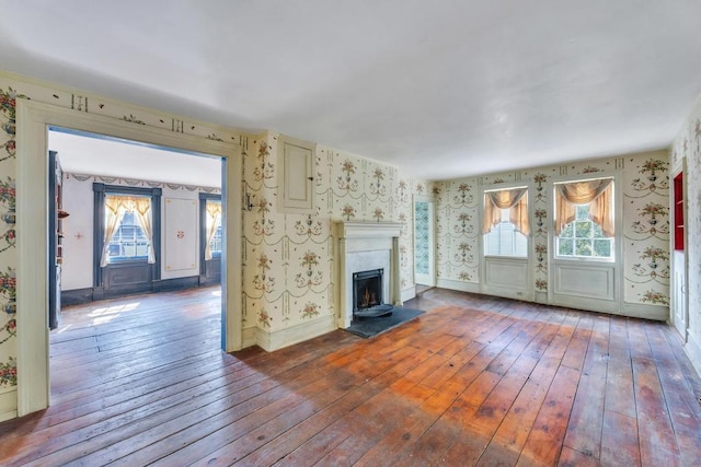 201 E Broadway Prt, Jefferson, NY 11777 - unfurnished living room featuring wallpapered walls, wood-type flooring, plenty of natural light, a fireplace with raised hearth, and baseboards