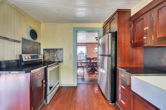 201 E Broadway Prt, Jefferson, NY 11777 - kitchen featuring stainless steel appliances, dark wood-style floors, dark countertops, reddish brown cabinets, and wood walls