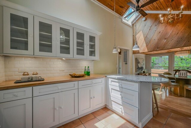 10 Maple Ave, Setauket, NY 11733 - kitchen featuring wood ceiling, high vaulted ceiling, light tile patterned floors, a peninsula, and glass insert cabinets