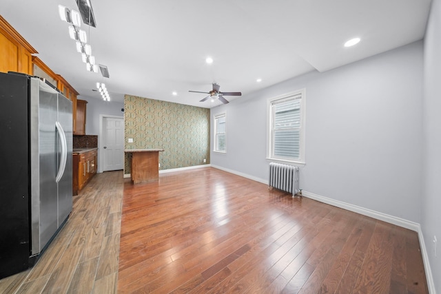 114-23 Sutter Ave, South Ozone Park, NY 11420 - unfurnished living room with radiator, wallpapered walls, ceiling fan, baseboards, and light wood-type flooring
