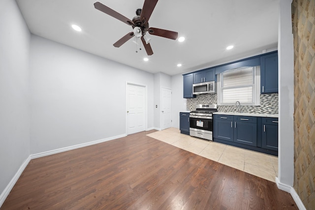 114-23 Sutter Ave, South Ozone Park, NY 11420 - kitchen featuring stainless steel appliances, ceiling fan, blue cabinetry, light countertops, and light wood-type flooring