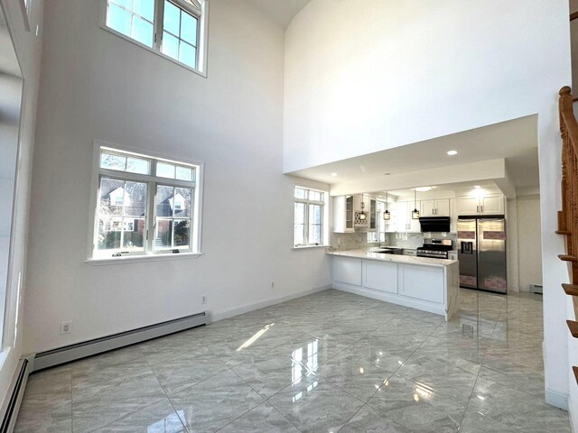36-46 205th St, Bayside, NY 11361 - unfurnished living room featuring light marble finish flooring, a high ceiling, baseboards, a sink, and a baseboard radiator