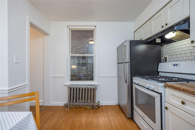 3496 Fort Independence St, Bronx, NY 10463 - kitchen with white gas stove, radiator heating unit, under cabinet range hood, backsplash, and baseboards