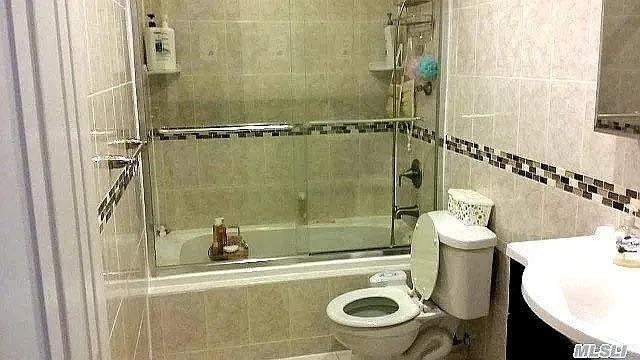 569 Peninsula Blvd, Cedarhurst, NY 11516 - full bath with bath / shower combo with glass door, toilet, tile walls, and vanity