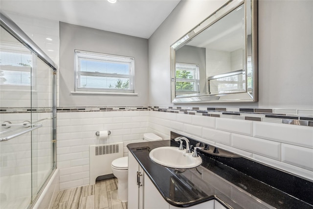 697 Byron Ave, Franklin Square, NY 11010 - bathroom featuring radiator heating unit, tile walls, toilet, bath / shower combo with glass door, and vanity