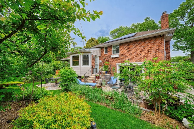 613 Gary Pl, Westbury, NY 11590 - back of house featuring entry steps, a patio, a chimney, solar panels, and brick siding