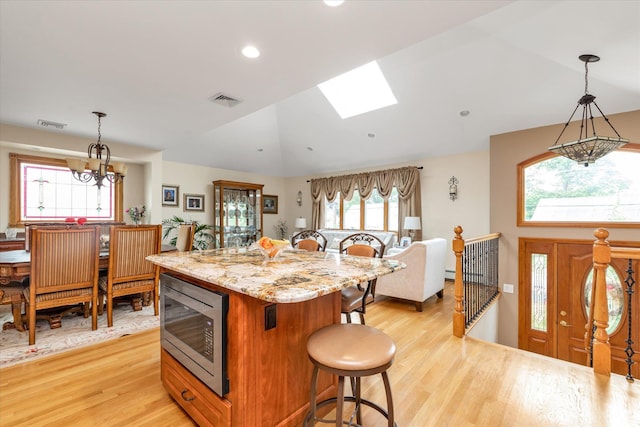 314 Oakview Ave, Oceanside, NY 11572 - kitchen with stainless steel microwave, a breakfast bar, light wood finished floors, a kitchen island, and a chandelier