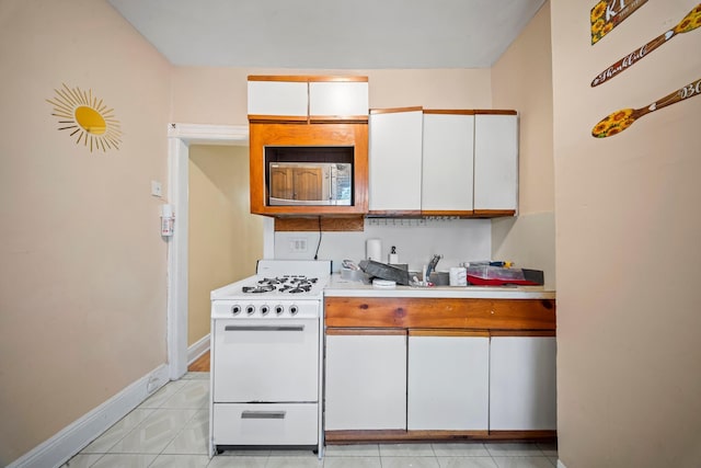 8564 79th St, Woodhaven, NY 11421 - kitchen featuring white range with gas stovetop, stainless steel microwave, light countertops, white cabinets, and light tile patterned flooring