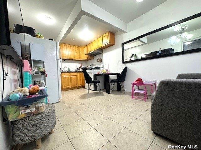 94-68 45th Ave, Elmhurst, NY 11373 - kitchen with light tile patterned floors, white appliances, brown cabinets, dark countertops, and under cabinet range hood