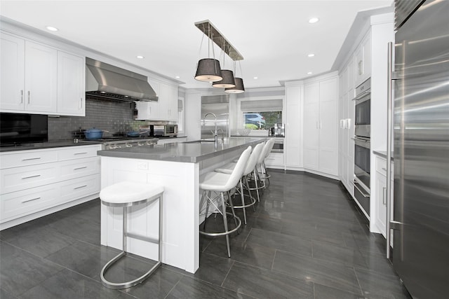 93 Haights Cross Rd, Chappaqua, NY 10514 - kitchen featuring appliances with stainless steel finishes, wall chimney range hood, a sink, a center island with sink, and white cabinets
