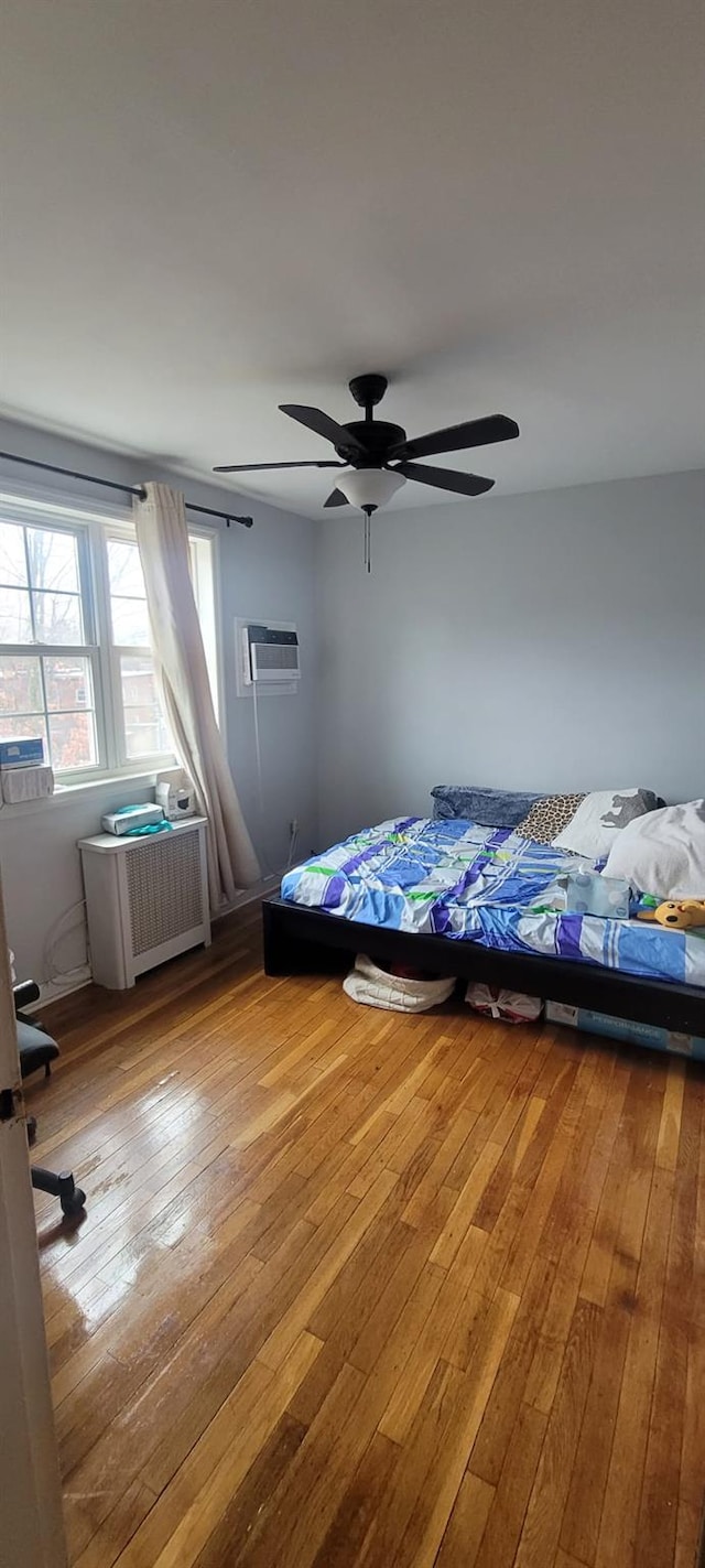 67-78 223rd Pl Unit B, Oakland Gardens, NY 11364 - bedroom with wood-type flooring, radiator, a wall mounted AC, and ceiling fan