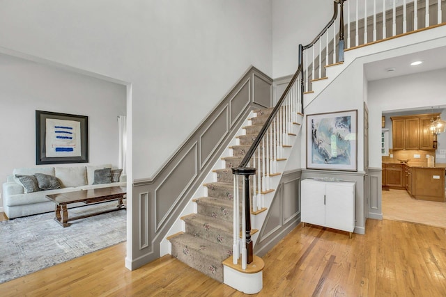 6 Esteves Ct, Melville, NY 11747 - staircase featuring a towering ceiling, wood finished floors, a decorative wall, and a wainscoted wall