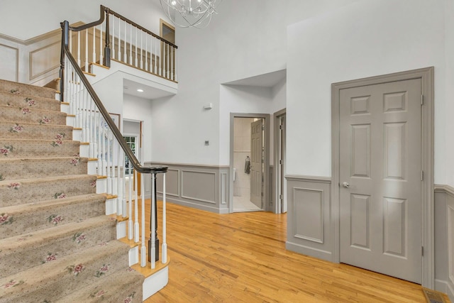 6 Esteves Ct, Melville, NY 11747 - stairs with a decorative wall, a wainscoted wall, wood finished floors, a towering ceiling, and a chandelier