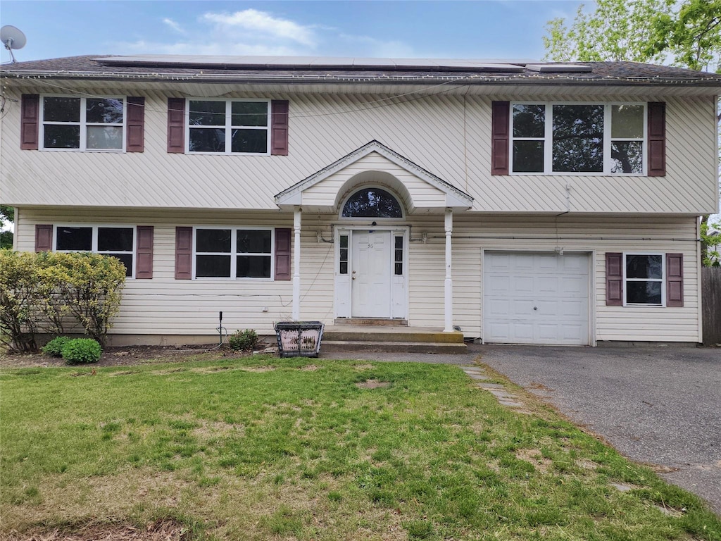36 S 23rd St, Wyandanch, NY 11798 - view of front of home with a front yard, a garage, driveway, and roof mounted solar panels