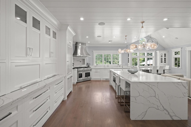 8 E Huxley Dr, Lloyd Harbor, NY 11743 - kitchen with wall chimney range hood, range with two ovens, a breakfast bar, white cabinetry, and dark wood-style flooring