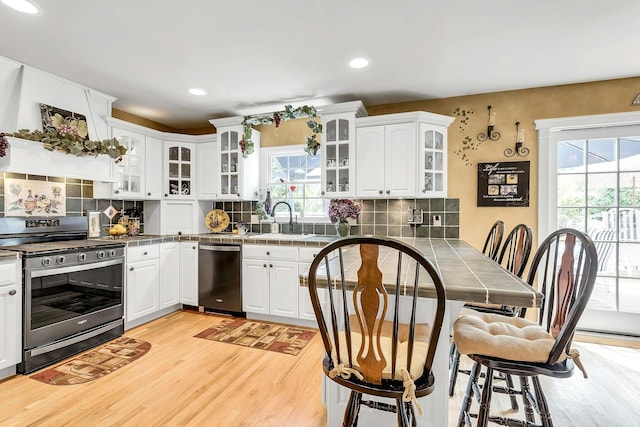 258 Timberpoint Rd, East Islip, NY 11730 - kitchen featuring appliances with stainless steel finishes, light wood-style floors, a sink, tile counters, and a breakfast bar