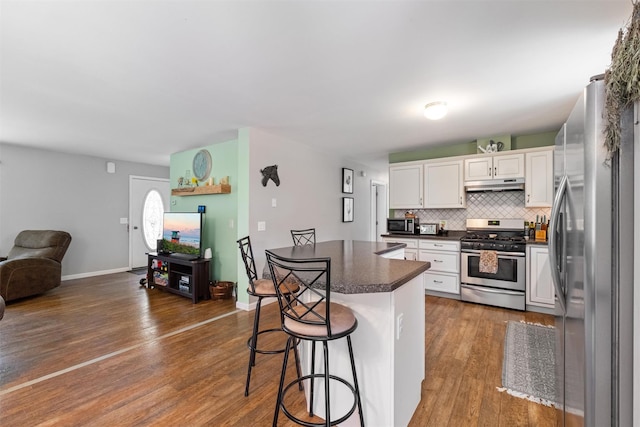 916 Queens Hwy, Accord, NY 12404 - kitchen with appliances with stainless steel finishes, under cabinet range hood, dark countertops, a kitchen bar, and dark wood-type flooring