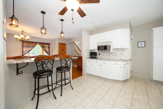 23 Saddle Rock Dr, Poughkeepsie, NY 12603 - kitchen with stainless steel microwave, a breakfast bar, ceiling fan, arched walkways, and decorative backsplash