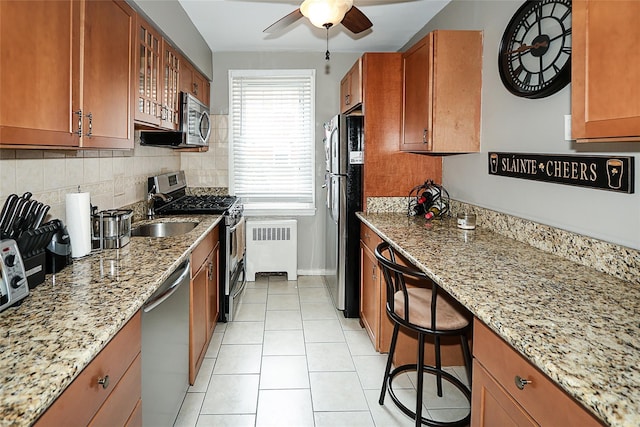 200 N Village Ave Unit D5, Rockville Centre, NY 11570 - kitchen with radiator, stainless steel appliances, a ceiling fan, brown cabinets, and glass insert cabinets