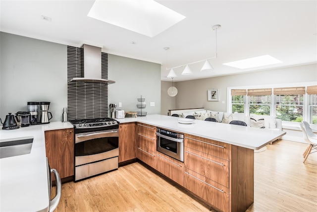 21 Hillside Dr W, Sag Harbor, NY 11963 - kitchen featuring a skylight, stainless steel appliances, wall chimney exhaust hood, a peninsula, and light wood-style floors