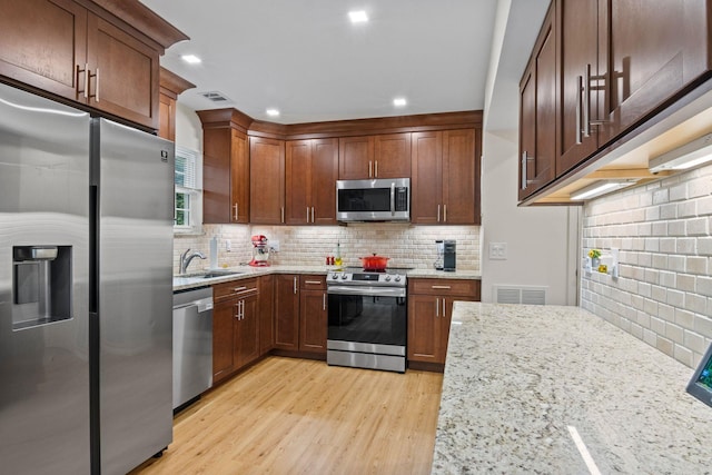 12 Franklin Commons, Yaphank, NY 11980 - kitchen with stainless steel appliances, light stone counters, tasteful backsplash, light wood-style floors, and a sink