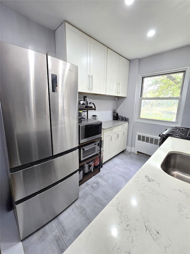 89-25 Shore Pkwy Unit 1L, Howard Beach, NY 11414 - kitchen featuring appliances with stainless steel finishes, radiator, white cabinetry, light stone countertops, and recessed lighting