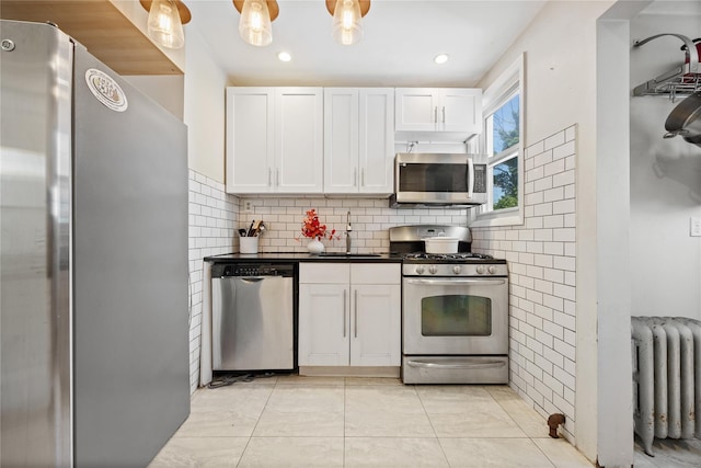 70-27 Olcott St, Forest Hills, NY 11375 - kitchen featuring appliances with stainless steel finishes, radiator heating unit, white cabinetry, dark countertops, and backsplash