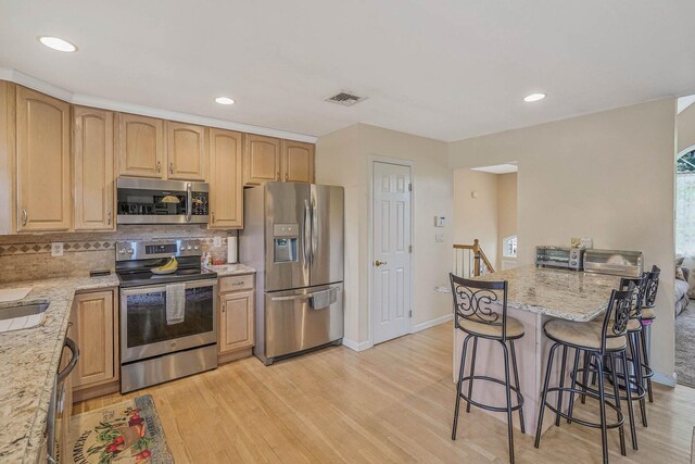 14 Arlington St, Patchogue, NY 11772 - kitchen featuring appliances with stainless steel finishes, a breakfast bar, light wood finished floors, tasteful backsplash, and light stone countertops