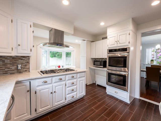 62 Webster Ave, Manhasset, NY 11030 - kitchen with appliances with stainless steel finishes, island range hood, backsplash, white cabinetry, and recessed lighting