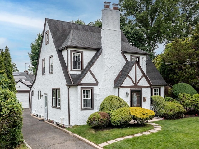 62 Webster Ave, Manhasset, NY 11030 - view of front of property with roof with shingles, a garage, a chimney, asphalt driveway, and a front lawn