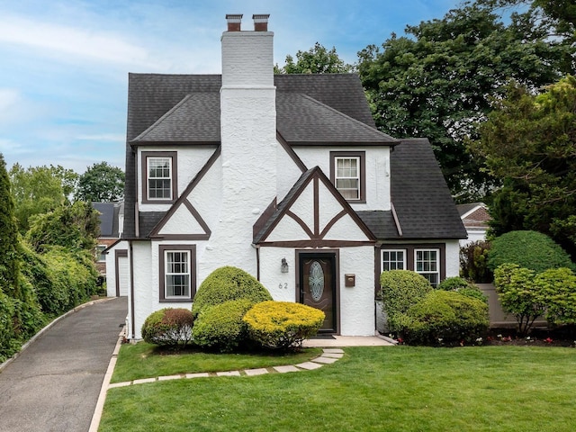 62 Webster Ave, Manhasset, NY 11030 - view of front facade featuring a front lawn, roof with shingles, a chimney, stucco siding, and asphalt driveway
