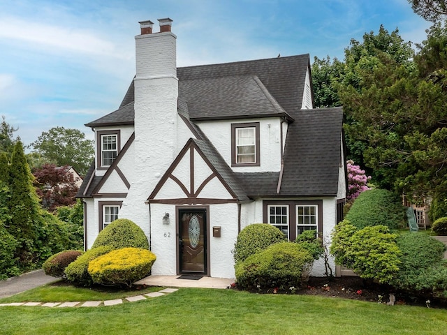 62 Webster Ave, Manhasset, NY 11030 - tudor home featuring a shingled roof, a front lawn, stucco siding, and a chimney
