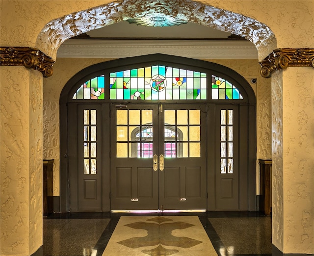 entrance foyer featuring granite floors, a textured wall, arched walkways, french doors, and baseboards